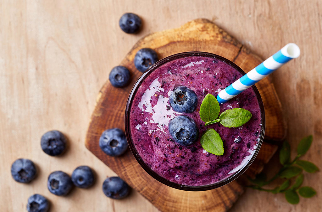 Glass of blueberry smoothie on wooden background from top view